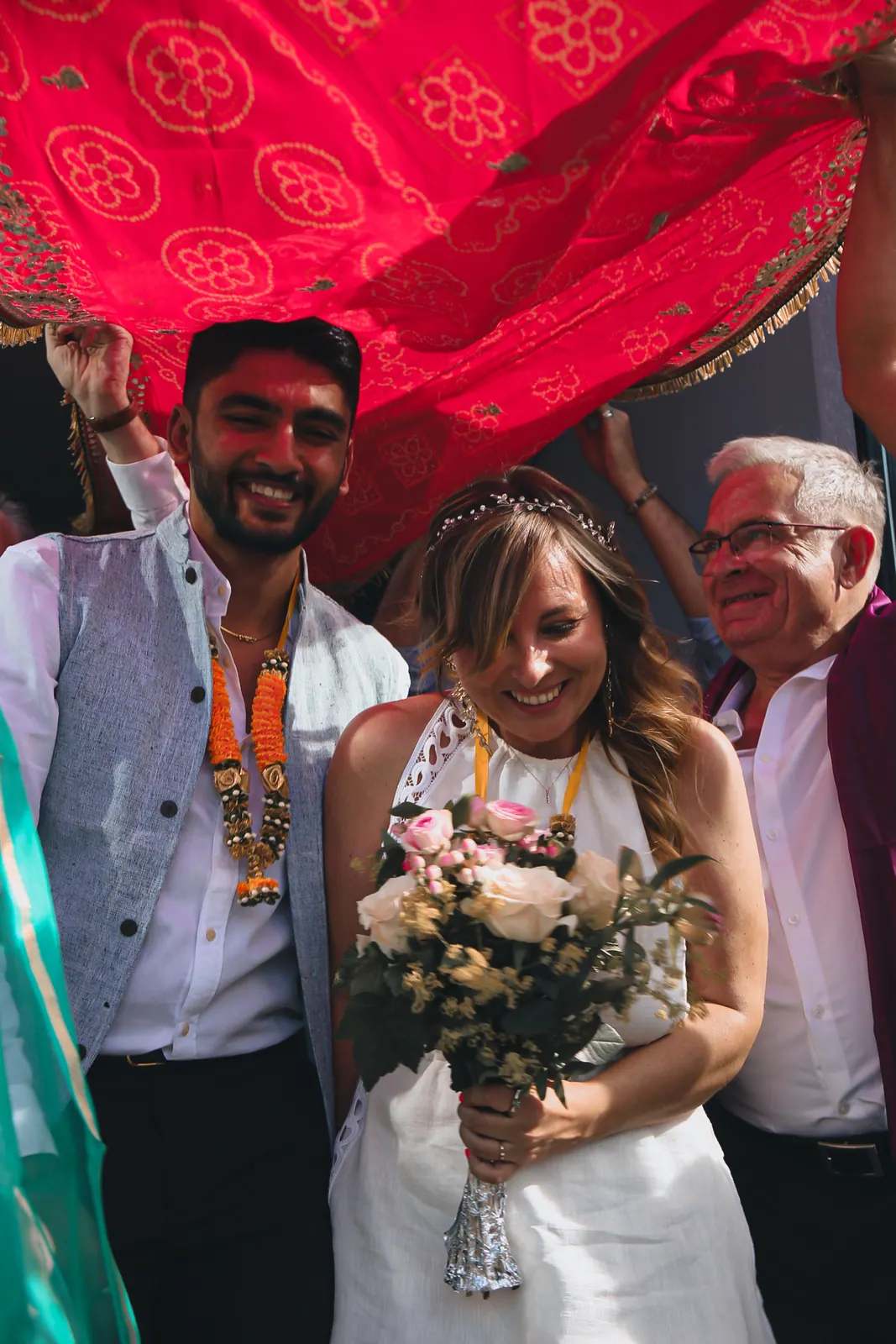Sortie des mariés sous un voile rouge tenu par la famille