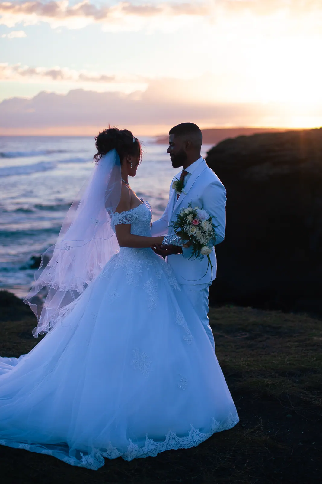 La robe de mariée s'étale sur la roche noire, les mariés face à face