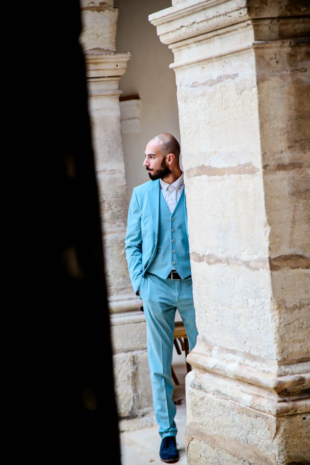 Clément adossé à une colonne en pierre, costume turquoise